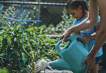 Girl watering plant in Anita's Garden Chelsea, MA